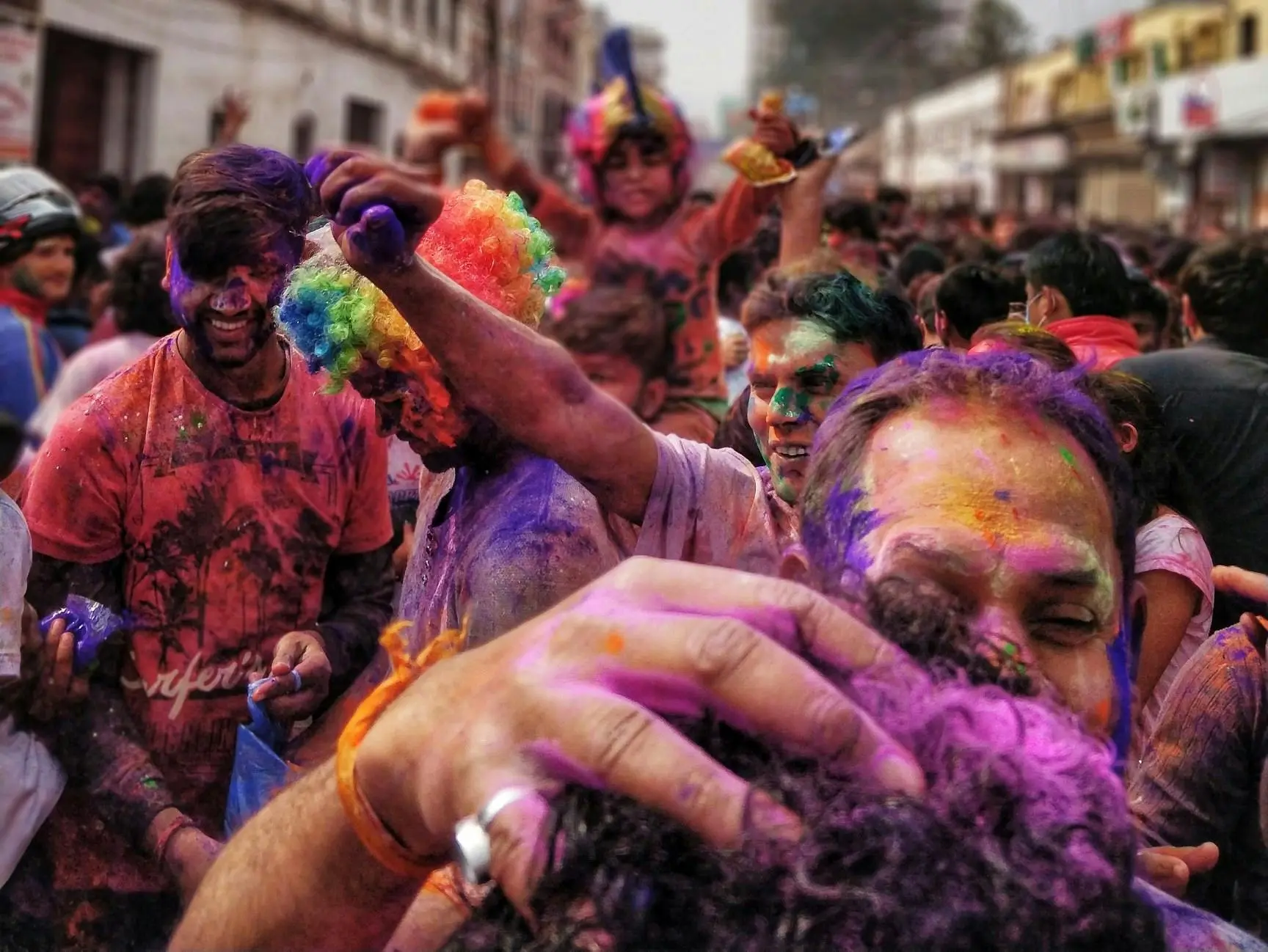 A joyful crowd celebrates during Holi festival, with people covered in vibrant colored powders.