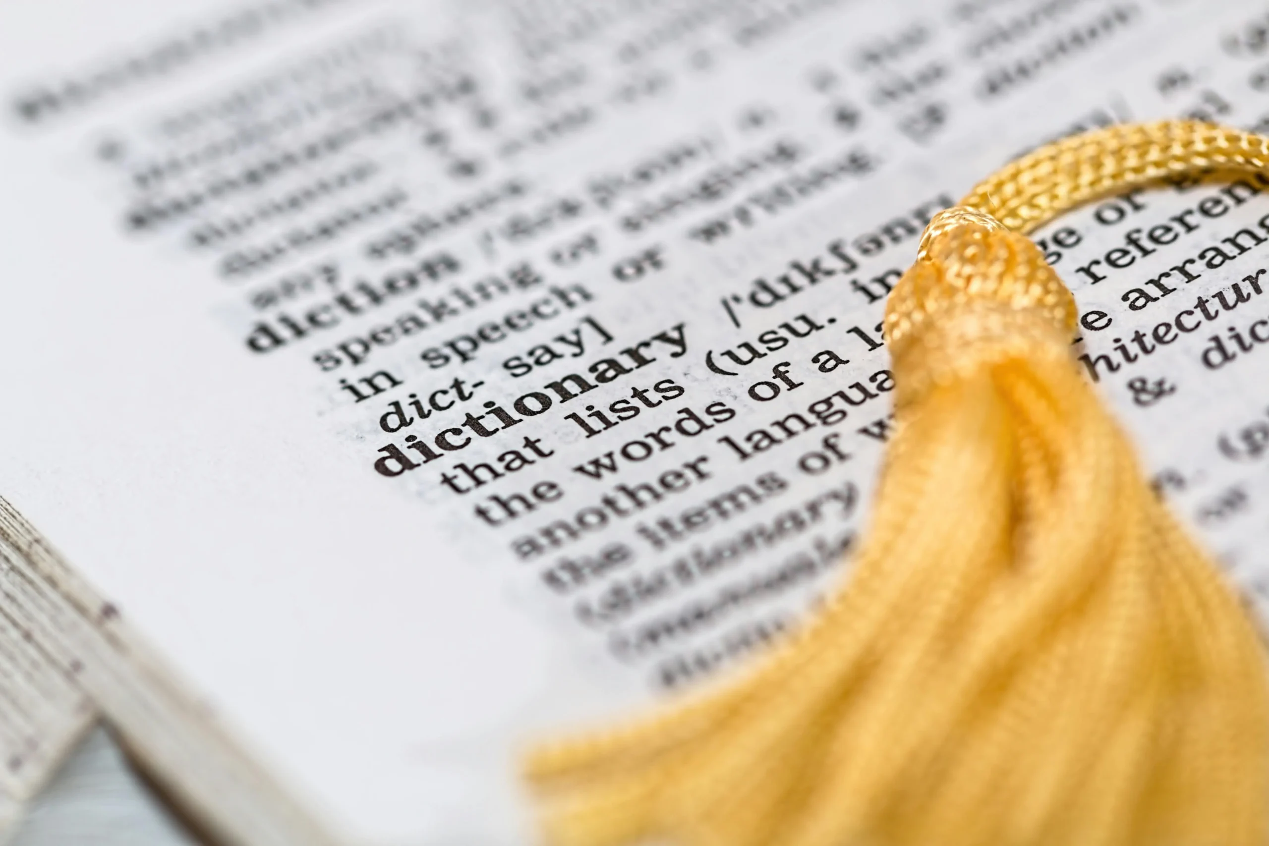 Close-up of a dictionary page focused on the word "dictionary," with a golden tassel resting on the page, symbolizing knowledge and learning.