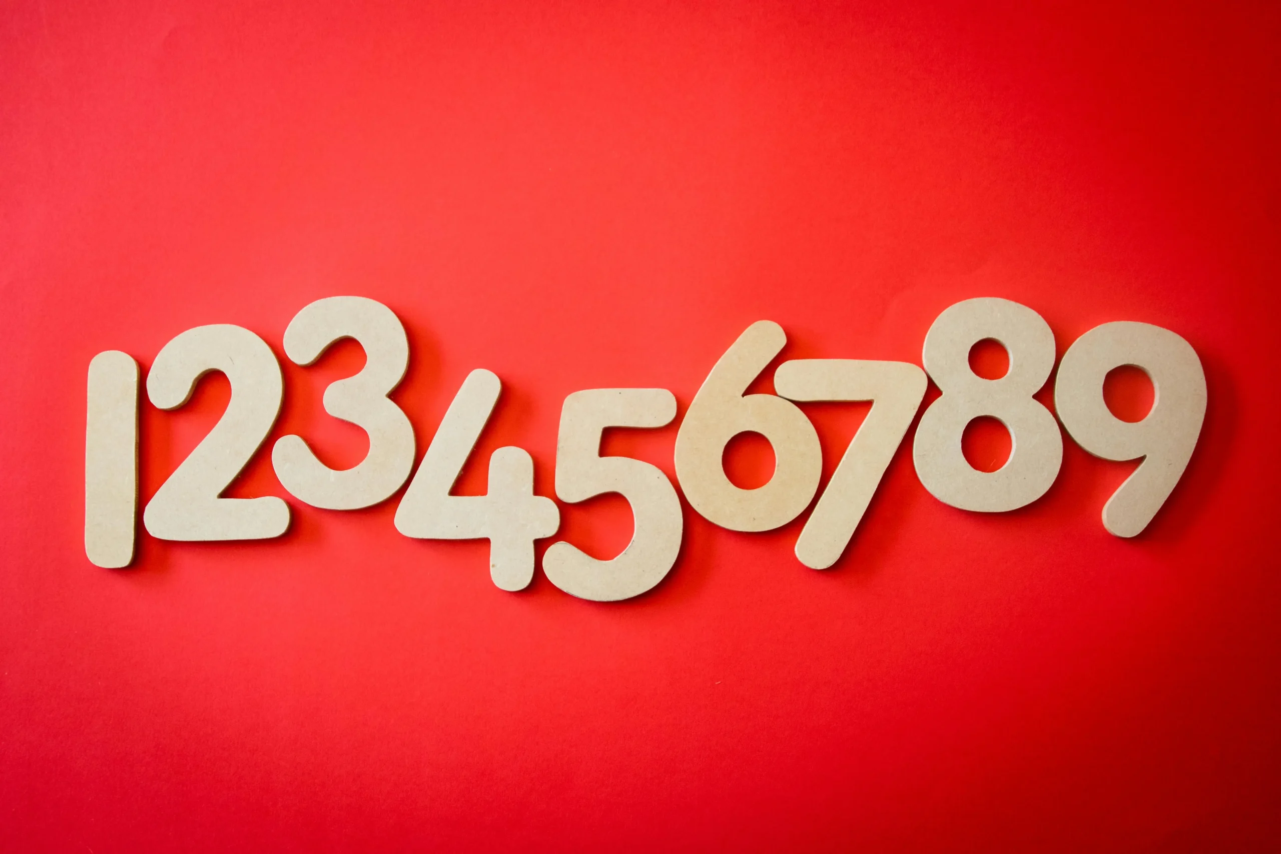 A sequence of large, beige wooden numbers (1 to 9) arranged horizontally on a bold red background, showcasing a clean and minimal design.